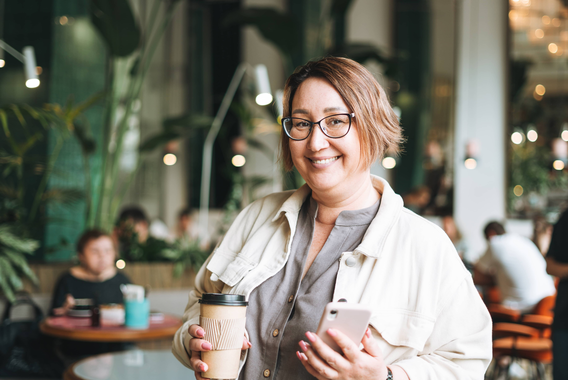 Persoon houdt een koffiebeker en smartphone vast