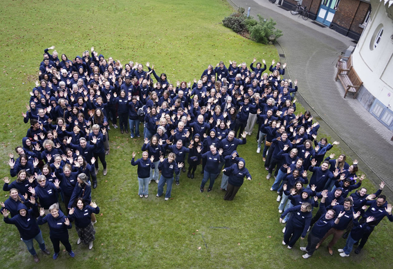 Groepsfoto van medewerkers van Emino die samen de letter M vormen op een grasveld