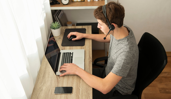 Jongen zit aan een bureau met een laptop en headset