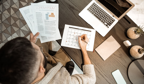 Persoon zit aan een bureau en bekijkt documenten terwijl een datum wordt aangeduid op een kalender