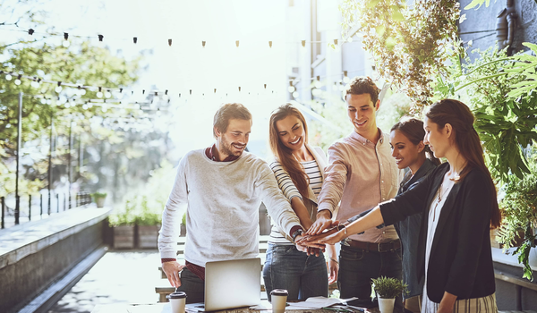 Vijf personen leggen hun handen samen rond een tafel